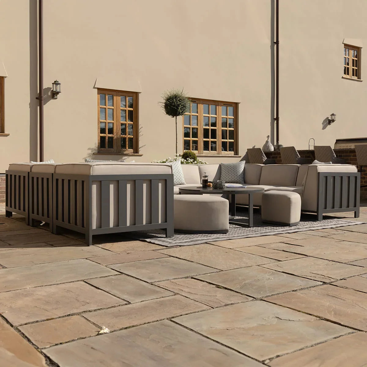 Grey outdoor corner sofa set with cushions and ottomans on stone patio