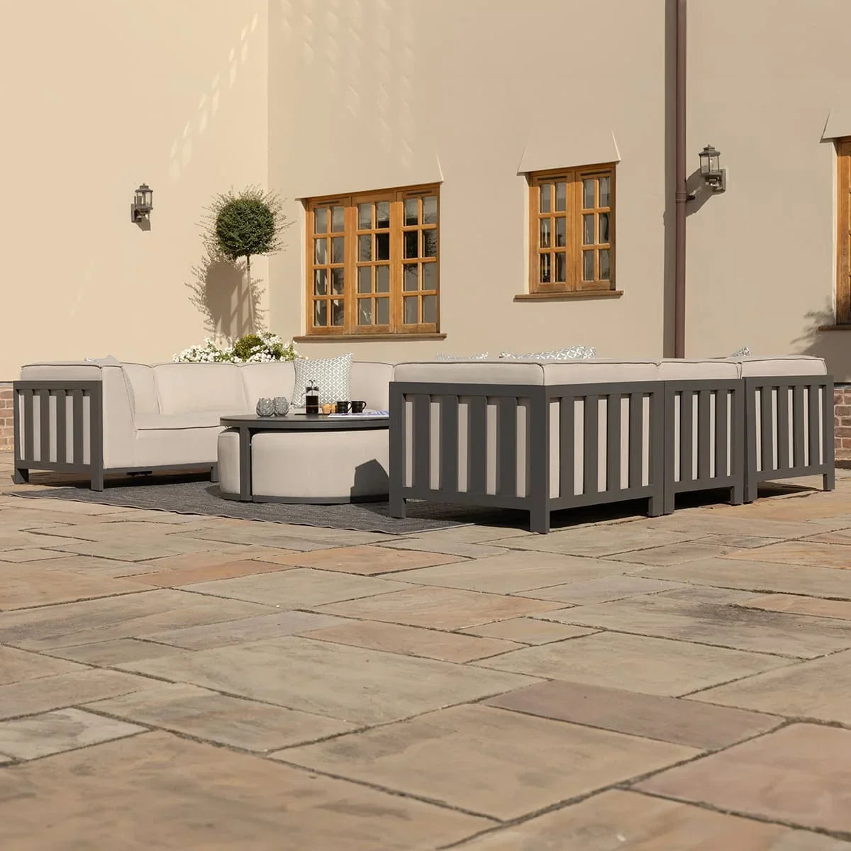 Grey outdoor sofa set with cream cushions and round coffee table on a stone patio