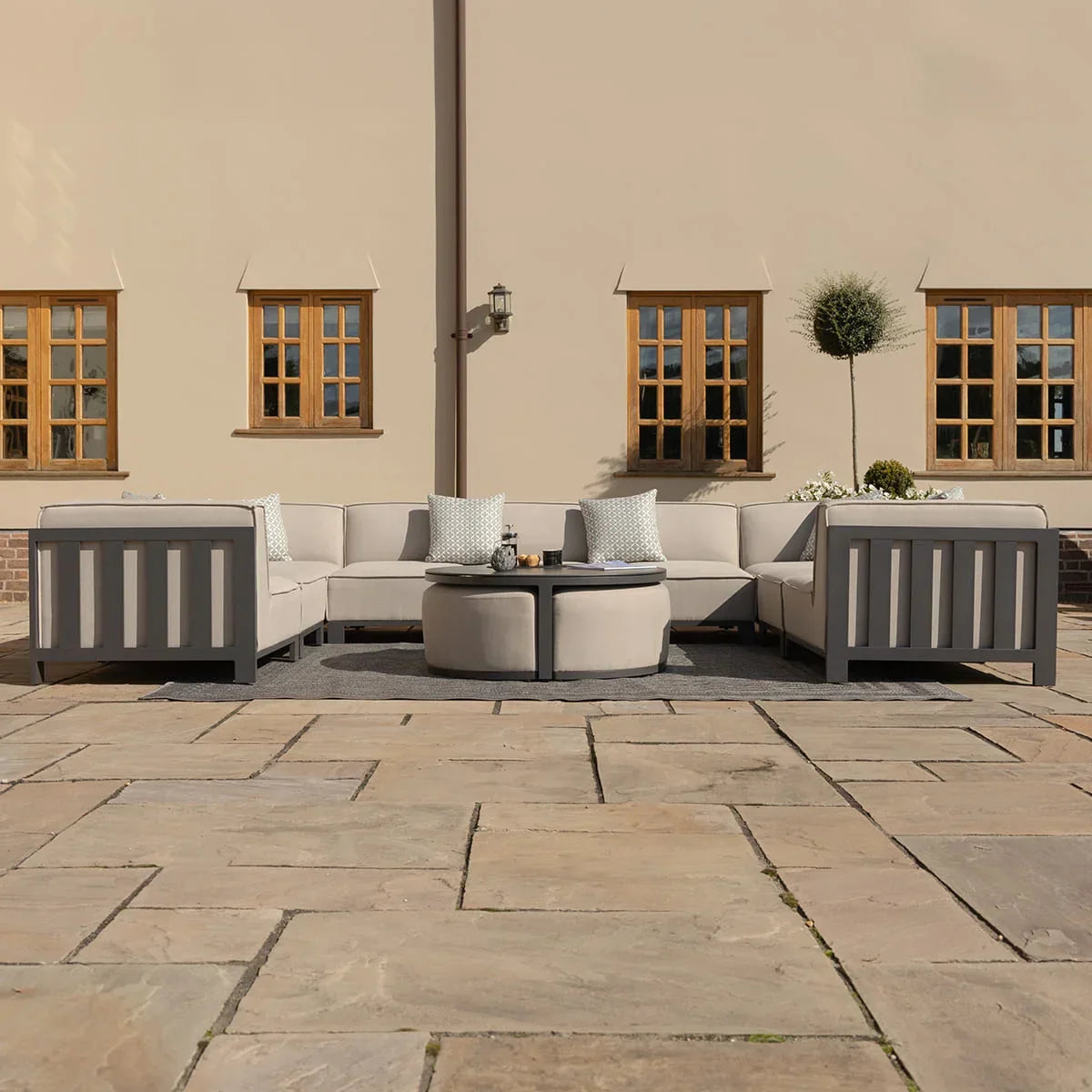 Grey outdoor corner sofa set with cushions and round coffee tables on stone patio