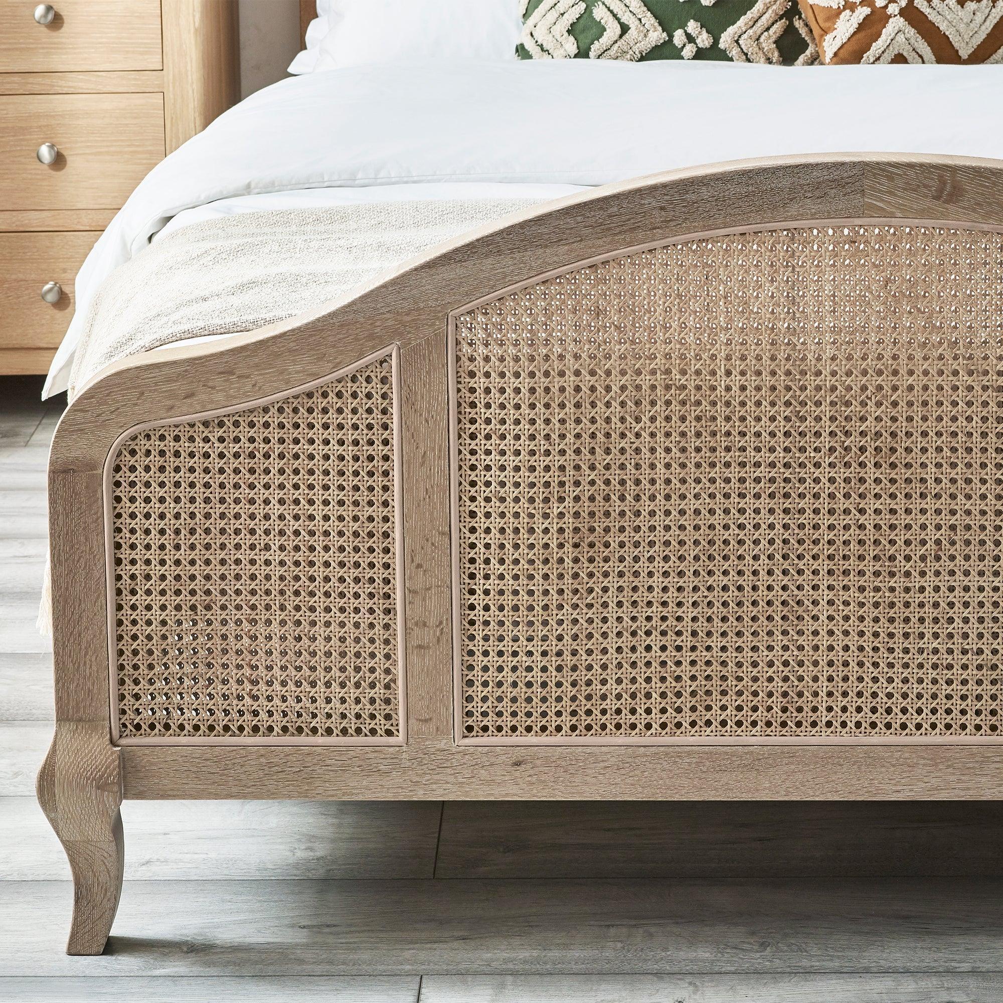 Natural rattan bed frame with curved footboard and wood legs in modern bedroom setting