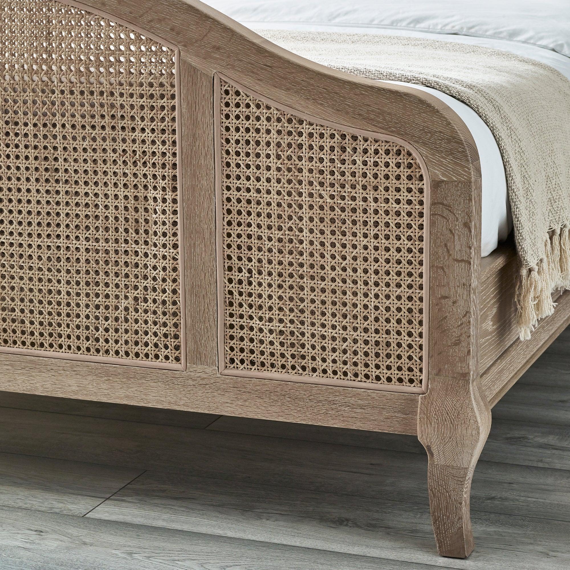 Wooden bed frame with woven rattan footboard panel and light oak finish on grey flooring
