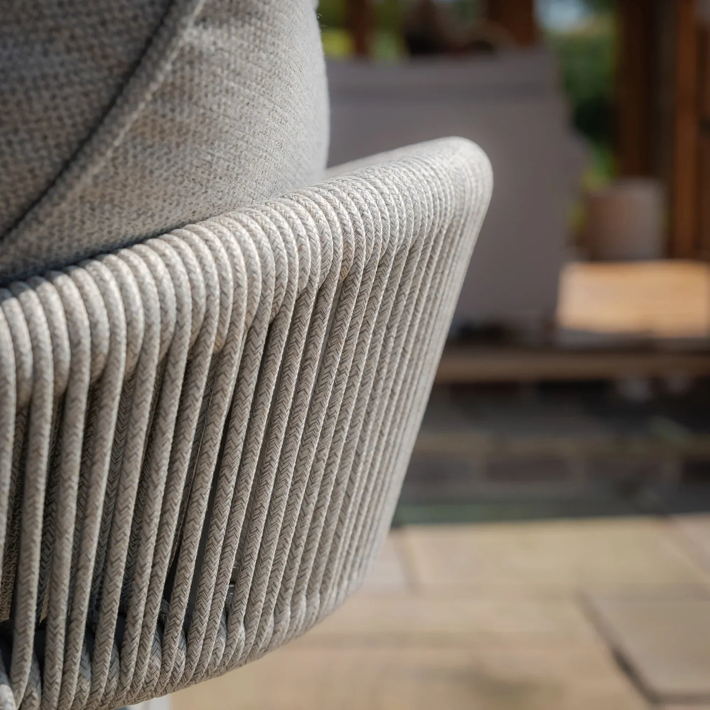 Close-up of beige rope woven outdoor sofa armrest with textured fabric cushion