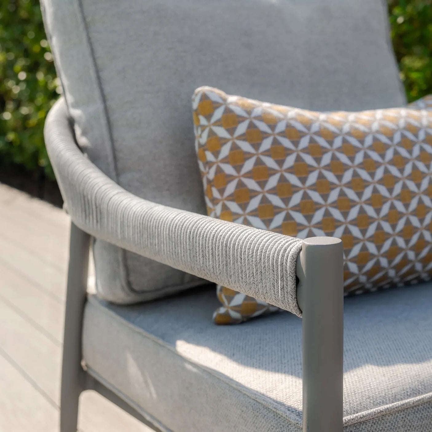 Light grey outdoor chair with rope arm detail, grey cushion, and geometric accent pillow