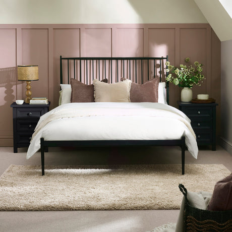 Black metal spindle bed with white bedding and beige pillows, flanked by dark nightstands and lamp