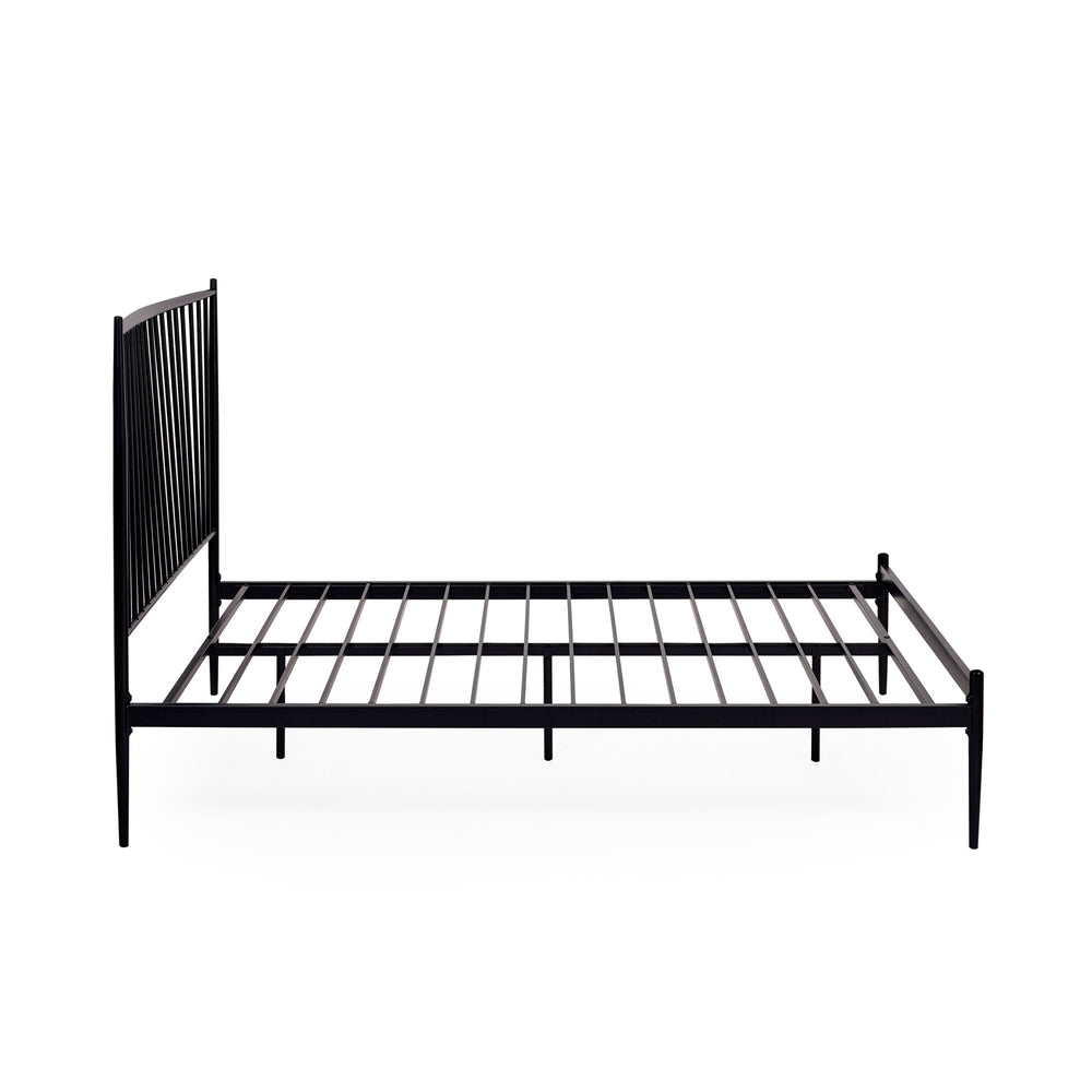 Close-up angled side view of black metal spindle bed with white bedding and beige pillows in soft light