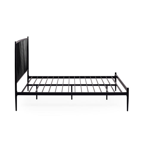Close-up angled side view of black metal spindle bed with white bedding and beige pillows in soft light