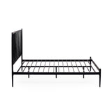 Close-up angled side view of black metal spindle bed with white bedding and beige pillows in soft light