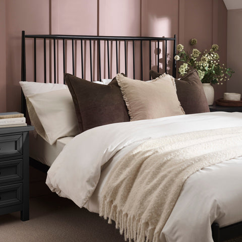 Close-up of black metal bed frame corner with white bedding and textured beige throw on beige carpet