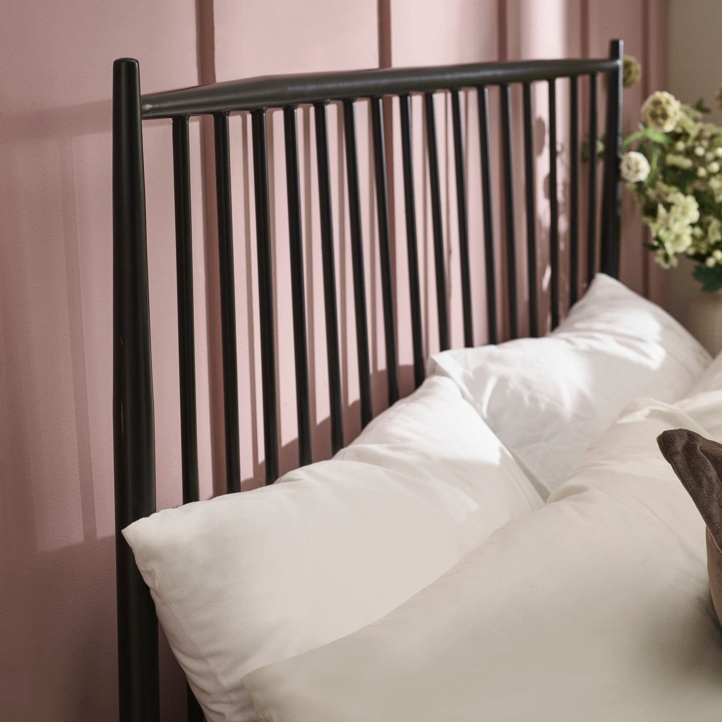 Close-up of pillow arrangement with white and beige pillows against black metal spindle headboard on muted pink wall