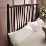 Close-up of pillow arrangement with white and beige pillows against black metal spindle headboard on muted pink wall