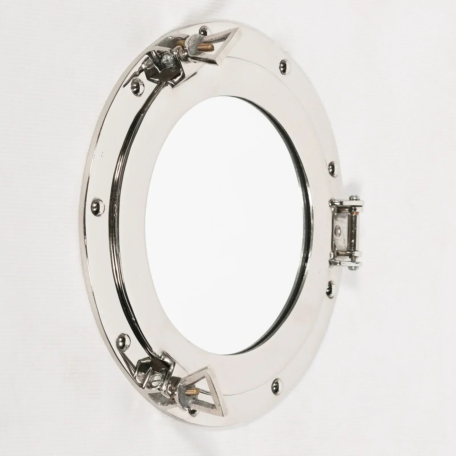 Polished chrome porthole mirror with round frame and hinge detail on white wall
