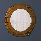 Round porthole wall mirror with brass frame mounted on dark blue wall