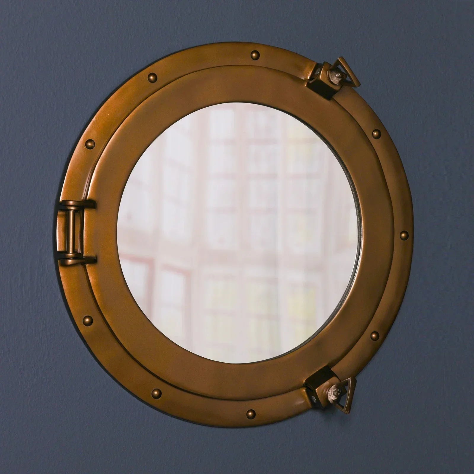 Round brass porthole wall mirror with rivet detail on dark blue wall