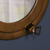 Close-up of brass porthole mirror frame with latch detail against blue wall