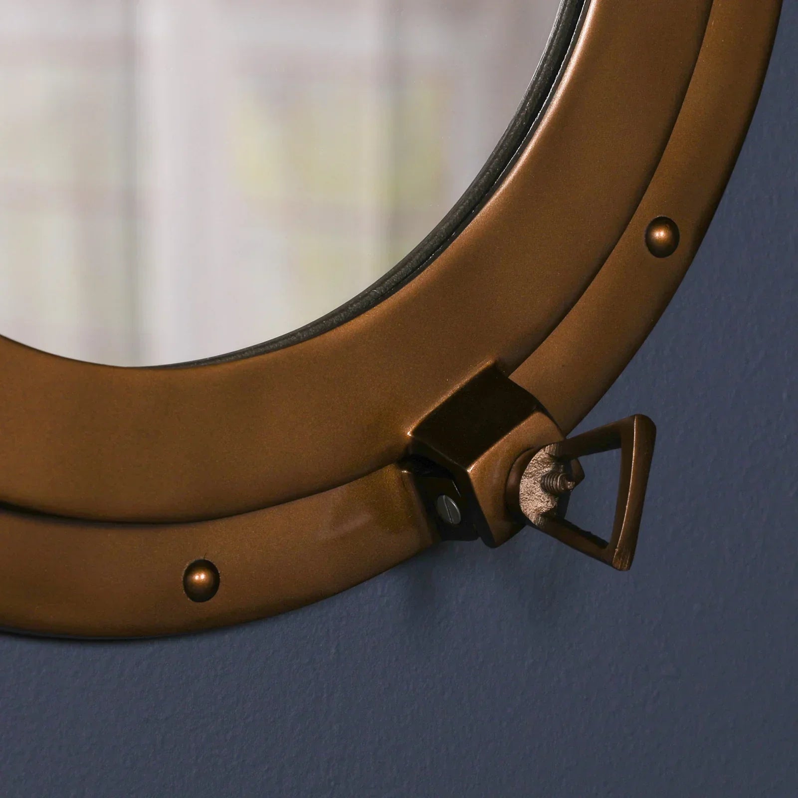 Close up of round brass wall mirror frame with latch detail against blue wall