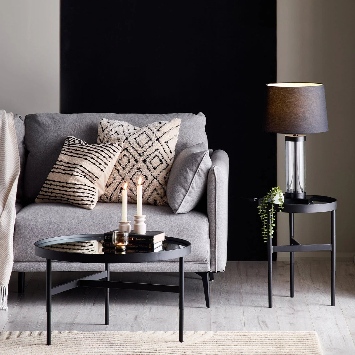 Grey fabric sofa with patterned cushions, black round coffee table and side table with lamp