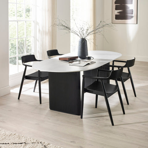 Six black wooden dining chairs with curved backs around white oval table in bright room with large window.