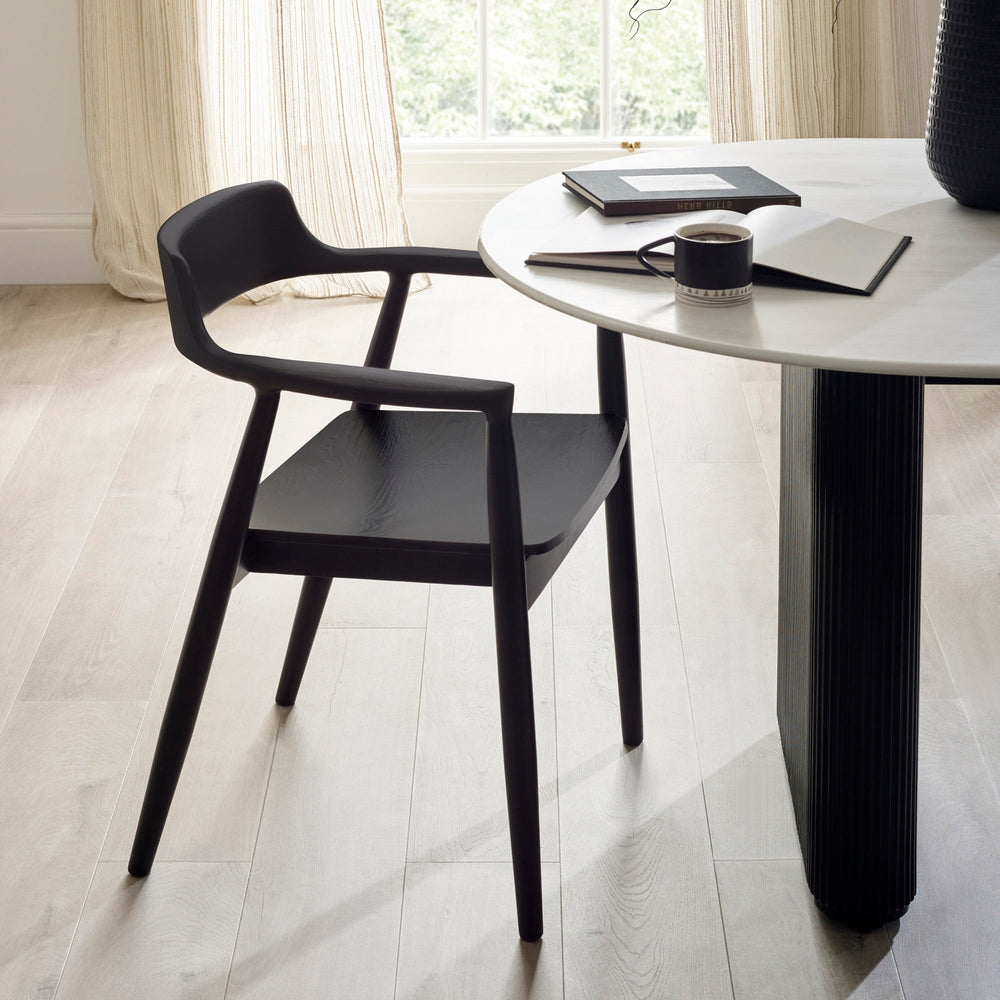 Single black wooden dining chair with rounded back and armrests beside white round table in bright room