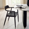 Single black wooden dining chair with rounded back and armrests beside white round table in bright room
