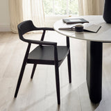 Single black wooden dining chair with rounded back and armrests beside white round table in bright room