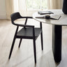 Single black wooden dining chair with rounded back and armrests beside white round table in bright room