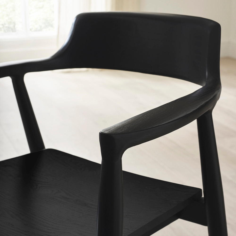 Close-up of rounded backrest and armrest on black wooden dining chair with visible wood grain texture