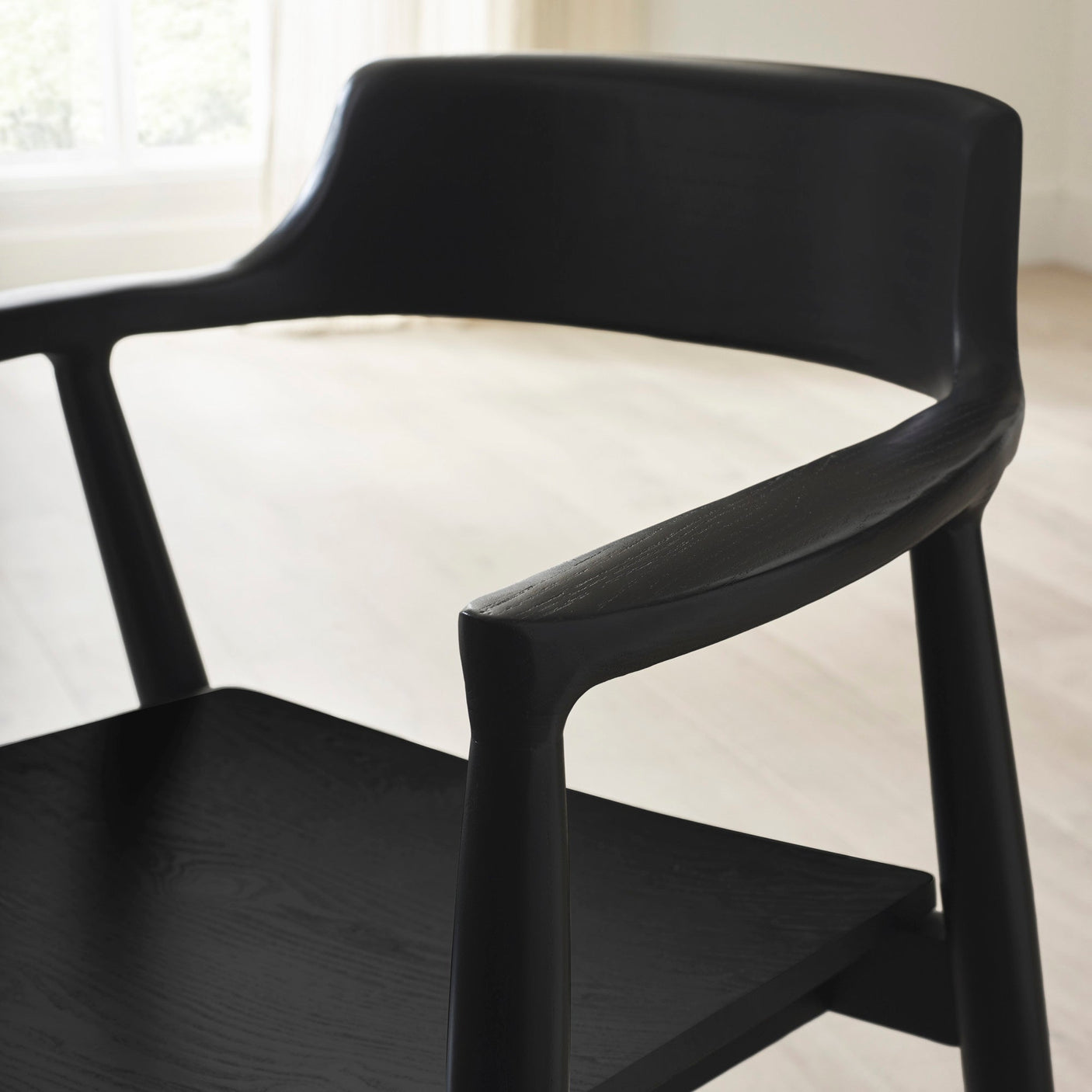 Close-up of rounded backrest and armrest on black wooden dining chair with visible wood grain texture