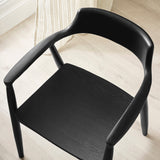 Close-up of black wooden dining chair with curved open backrest and armrests on light wood floor.
