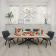 A modern dining room scene with a rectangular light wood table surrounded by six black quilted chairs. The table is set with colorful drinks, fruit, and small plates of food.