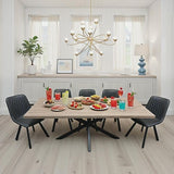 A modern dining room scene with a rectangular light wood table surrounded by six black quilted chairs. The table is set with colorful drinks, fruit, and small plates of food.