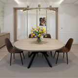 A round light wood dining table with a black metal pedestal base, surrounded by four dark brown chairs, in a modern dining room setting with a floral centerpiece and a large circular chandelier overhead.