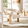Cream boucle fabric accent armchair with rounded backrest, oak legs on a textured cream rug in bright room.