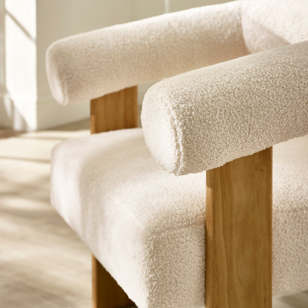 Close-up of cream boucle fabric upholstery on arm and seat cushion with oak legs in natural lighting.