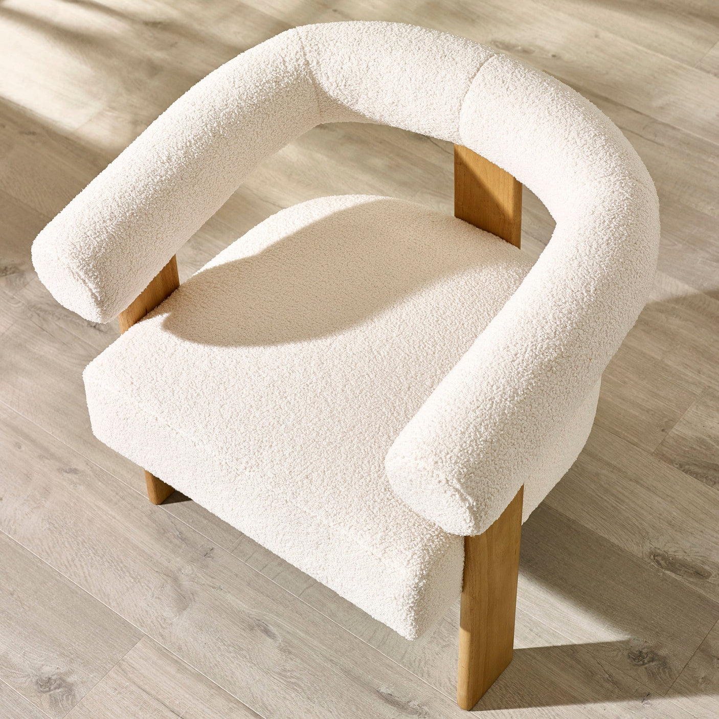 Top angled view of cream boucle accent chair highlighting rounded backrest, thick seat cushion and oak legs.