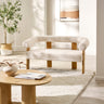 Cream boucle fabric 2 seater sofa with rounded backrest and light wood frame in bright living room