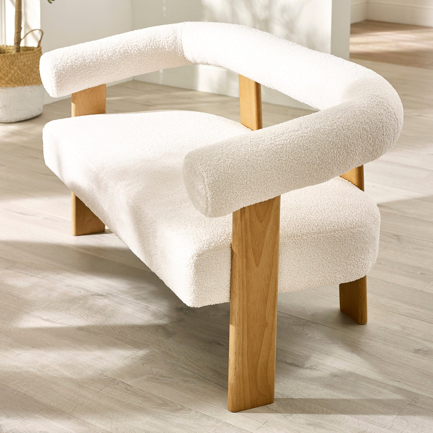 Close-up angled shot of cream boucle 2 seater sofa showing armrest, curved backrest and light wood frame