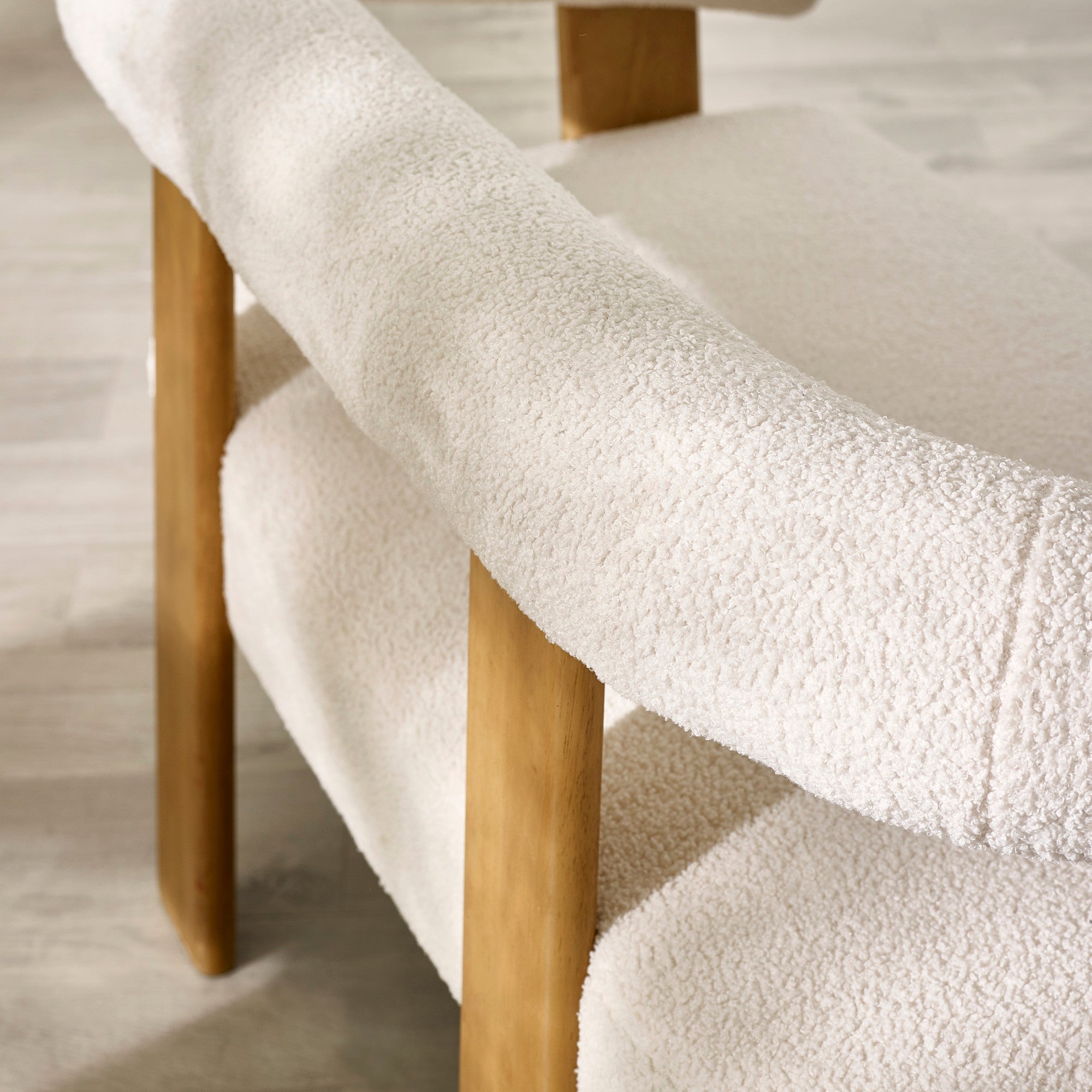 Close-up of cream boucle fabric curved armrest and backrest with solid light wood backing and leg