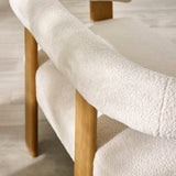 Close-up of cream boucle fabric curved armrest and backrest with solid light wood backing and leg