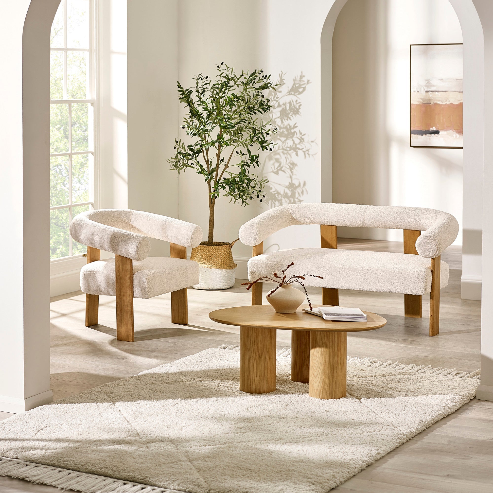 Cream boucle 2 seater sofa with wooden legs and curved armrest in bright room with light wood table and plant