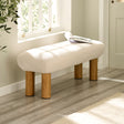 Cream upholstered low bench with cylindrical wooden legs beside a window with sunlight.