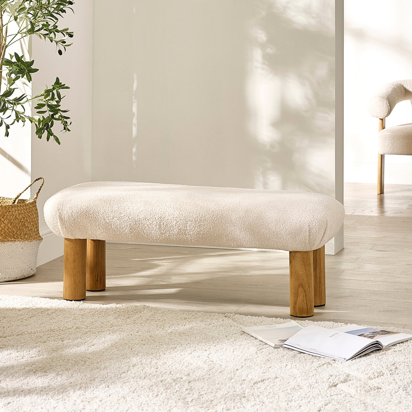 Low bench with cream soft fabric and wooden legs next to woven basket and rug in bright room.