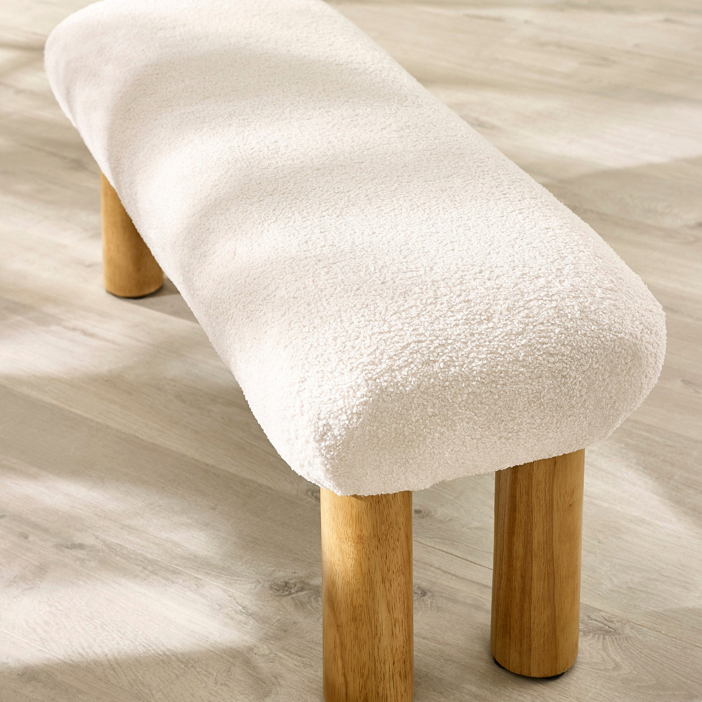 Close-up of low bench with cream textured fabric upholstery and rounded natural wooden legs on light wood floor