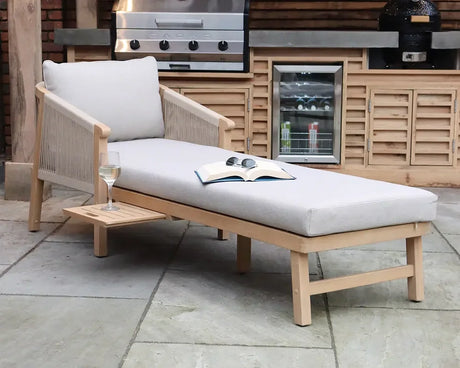 Wooden garden lounger with grey cushion, side table, book and drink on patio