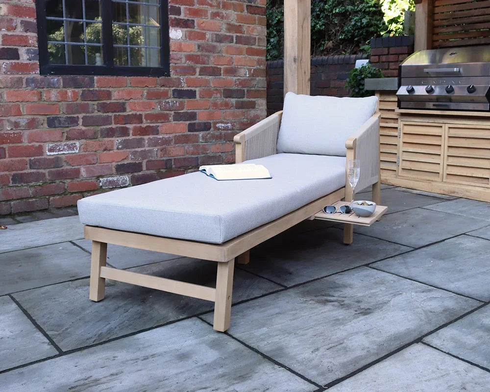 Outdoor wooden sun lounger with cushion and side tray on stone patio