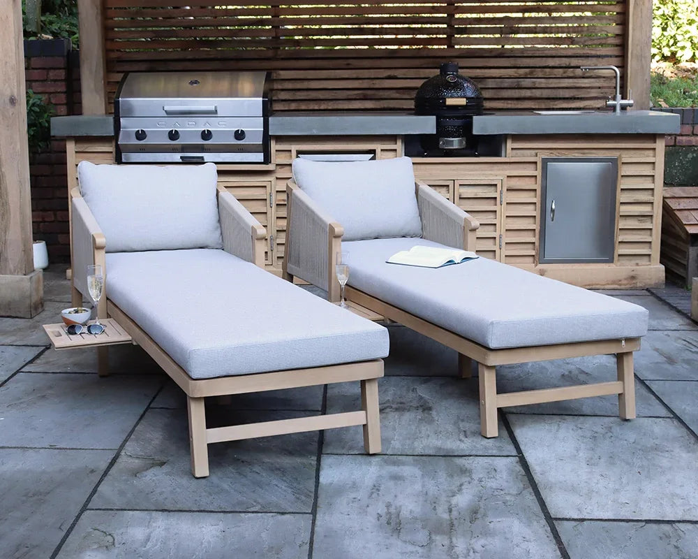 Outdoor wooden sun loungers with light grey cushions beside a patio kitchen and grill