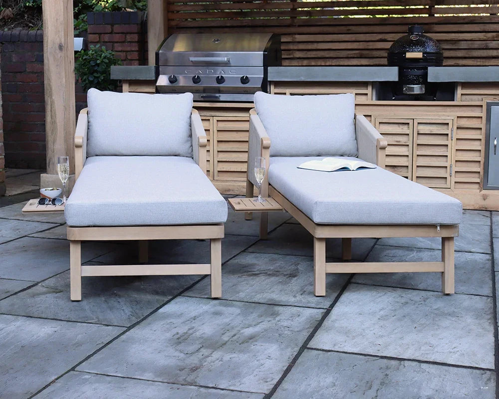 Pair of outdoor wooden sun loungers with grey cushions and built-in side tables on patio