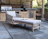 Grey cushioned garden lounger with wooden frame on patio beside outdoor kitchen grill