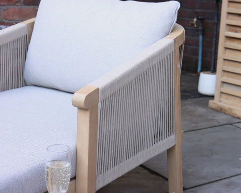 Light grey cushioned outdoor armchair with rope sides on patio, glass of sparkling drink on armrest