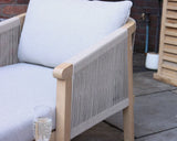 Light grey cushioned outdoor armchair with rope sides on patio, glass of sparkling drink on armrest