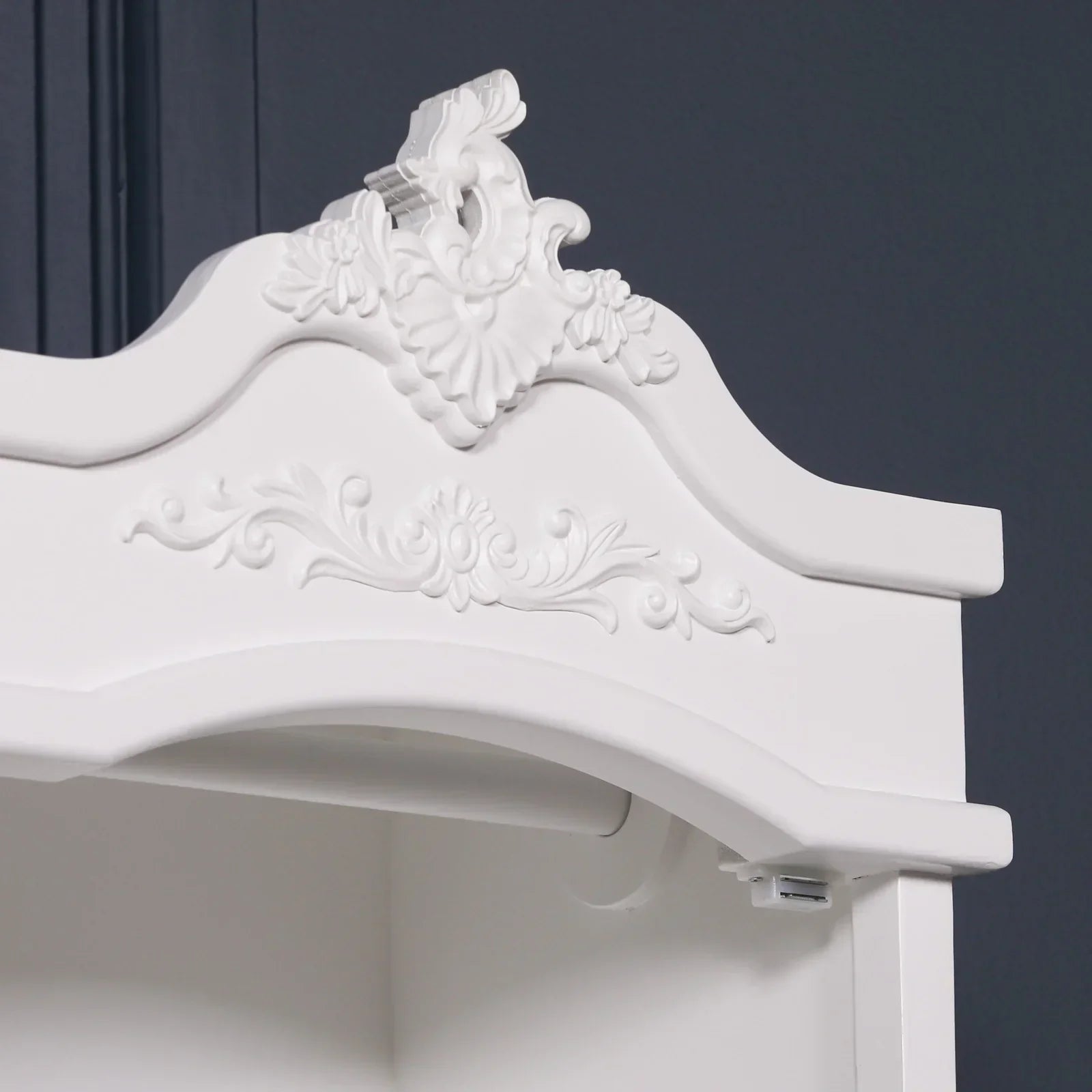 White wooden wardrobe with ornate carved detailing on the top cornice